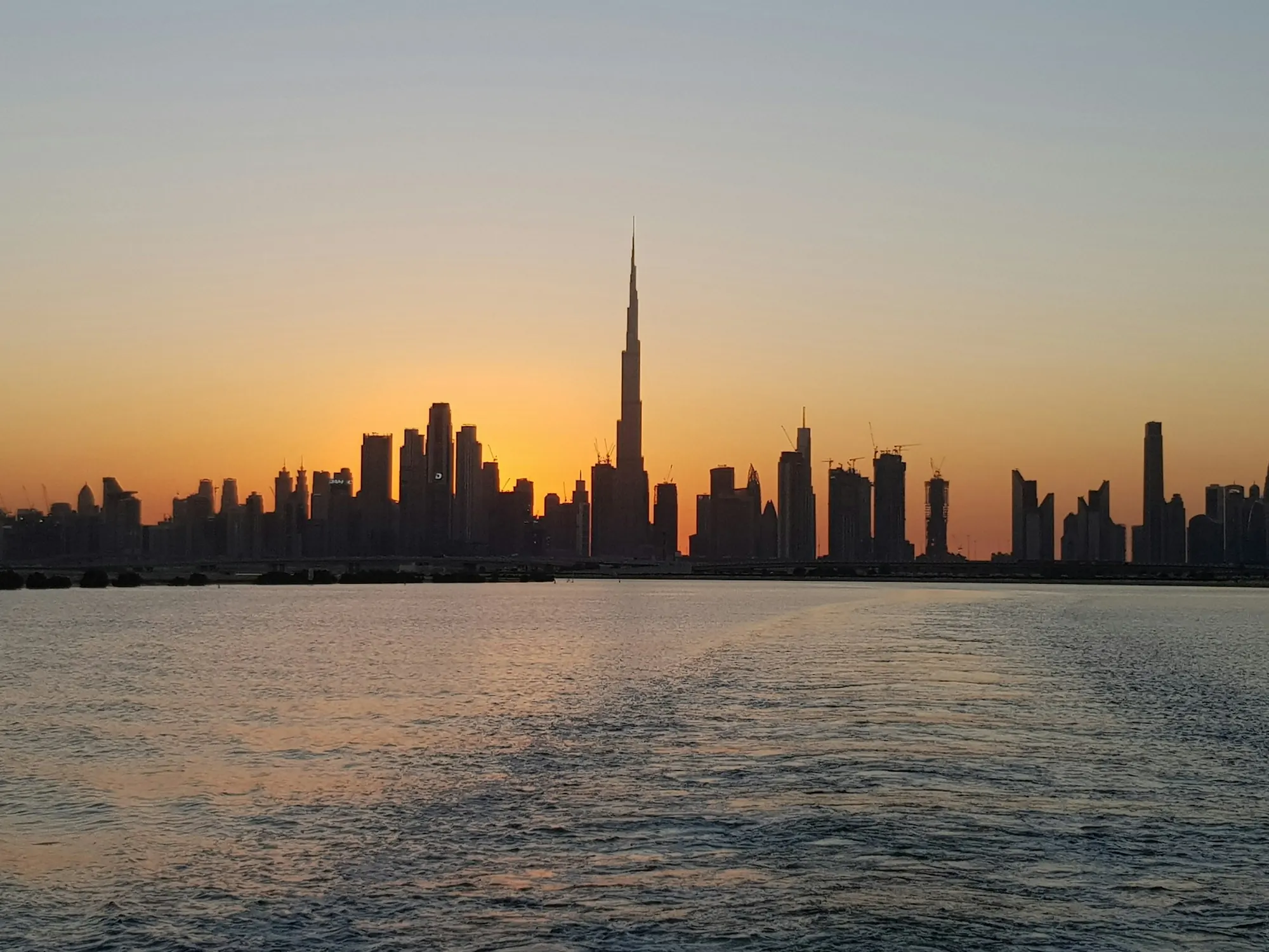Dubai skyline silhouetted against an orange sunset over the water